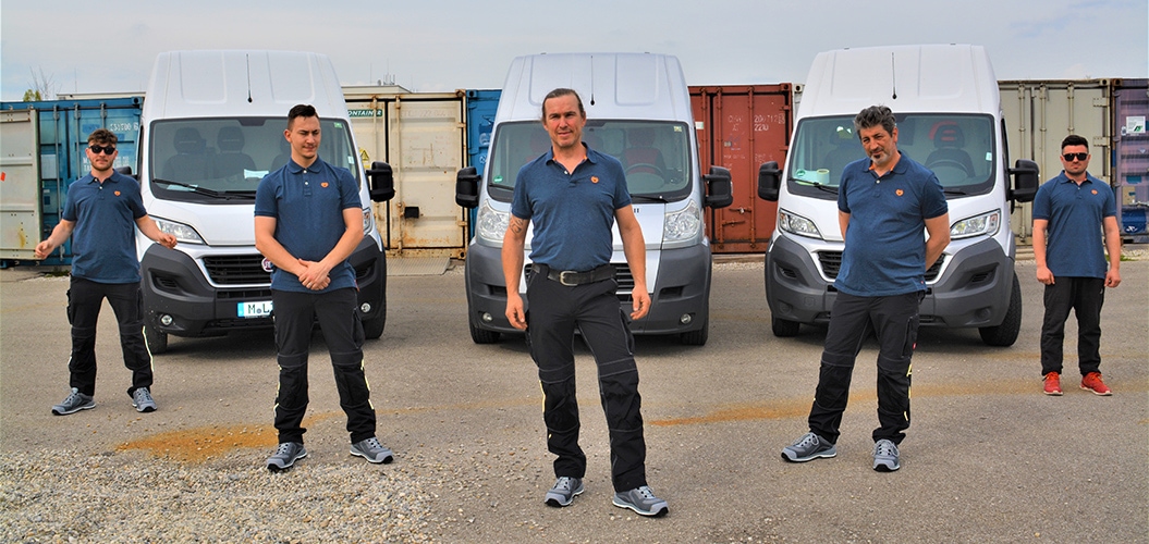 Team in Arbeitskleidung vor der Fahrzeugflotte